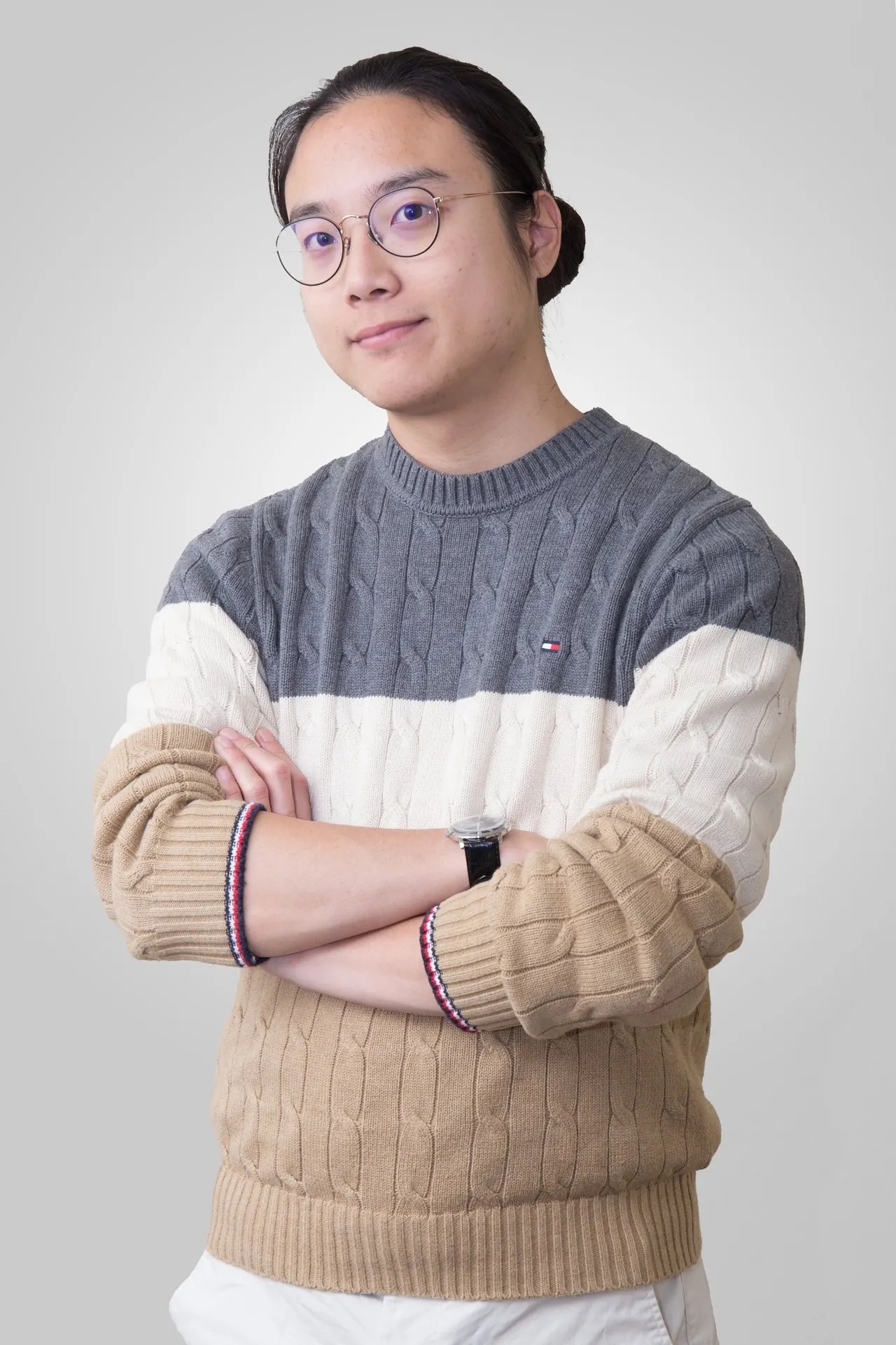 Portrait of Aaron in a striped cable-knit sweater, arms crossed, with a calm half-smile against a pale grey backdrop.